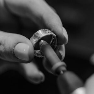 Detailed black and white photo of an artisan polishing a ring with precision tools.